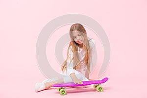 Loving her penny board. Little girl putting hand on board deck on pink background. Adorable small skater with violet