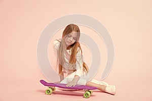 Loving her penny board. Little girl putting hand on board deck on pink background. Adorable small skater with violet