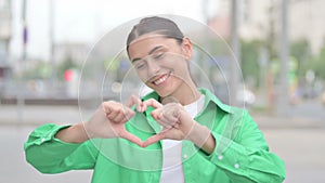 Loving Hispanic Woman showing Heart Shape by Hands Outdoor