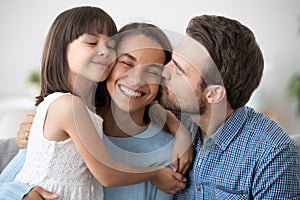 Loving husband and cute kid daughter embracing kissing happy wom