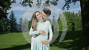 Loving husband gently kissing his beautiful pregnant wife in sunlit green garden