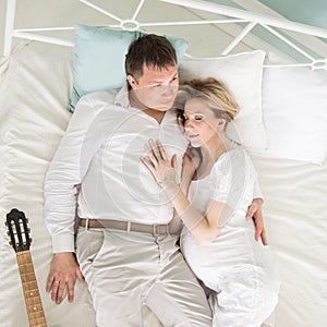 Loving husband with a guitar and his pregnant wife on the bed in