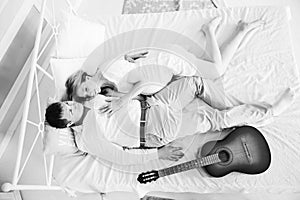 Loving husband with a guitar and his pregnant wife in bed in beautiful interior