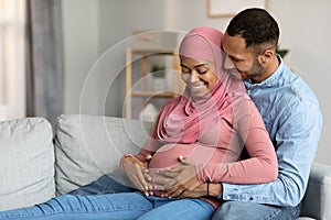 Loving Husband Hugging Pregnant Muslim Wife While Relaxing On Couch At Home