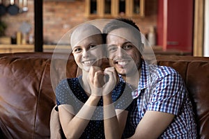 Loving husband hugging wife cancer patient on sofa at home