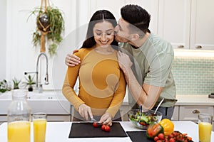 Loving husband kissing his attractive wife while cooking at home