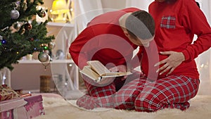 Loving husband reading book to belly of unrecognizable pregnant wife and kissing fetus. Portrait of happy Caucasian man