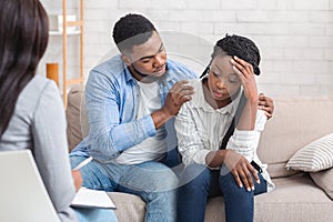 Loving husband supporting his depressed wife during psychotherapy session with counselor photo