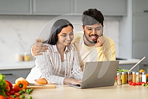 Loving indian couple cooking together, checking recipes on Internet