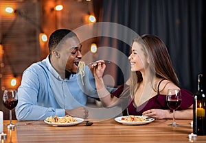 Loving Interracial Couple Feeding Each Other With Spaghetti During Dinner In Restaurant
