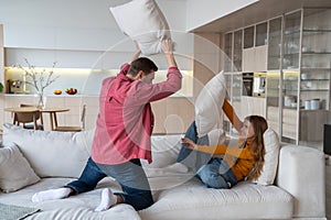 Loving joyful couple fool around spending pastime childishly at home, fighting with pillows, amusing