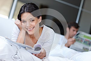 Loving the latest fashions. a beautiful woman lying in bed enjoying a magazine.