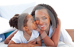 Loving little girl kissing her mother lying on bed