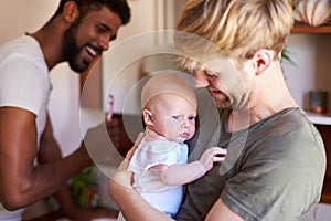 Loving Male Same Sex Couple Cuddling Baby Daughter In Bathroom At Home Together