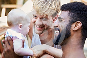 Loving Male Same Sex Couple Cuddling Baby Daughter At Home In Garden Together