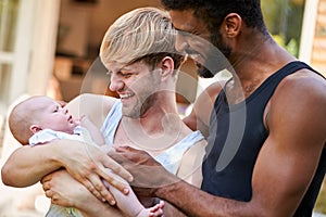 Loving Male Same Sex Couple Cuddling Baby Daughter At Home In Garden Together