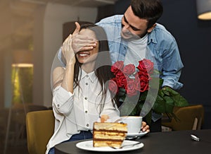 Loving Man Covering Girlfriend`s Eyes Giving Her Bouquet In Cafe