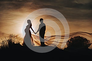 Loving man hugs a pregnant woman at sunset, against the backdrop of the sea, river, standing on the pier. Portrait of