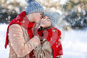 Loving man kissing his pretty girlfriend while enjoyng snowy weekend