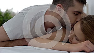 Loving man kissing his sleeping girlfriend with tenderness in morning, honeymoon