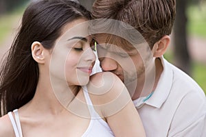 Loving man kissing woman shoulder with tenderness in park