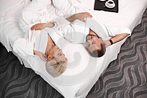 Loving married couple lie on bed in hotel, relax