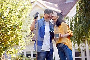 Loving Mature Asian Couple Taking A Break With Hot Drinks Whilst Tidying Garden With Rake