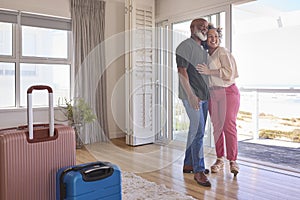 Loving Mature Couple With Luggage Arriving In Beachfront House Overlooking Ocean For Summer Vacation photo