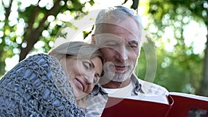 Loving mature family watching photoalbum, remembering childhood of their kids