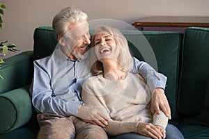 Loving middle aged husband embracing laughing wife, sitting on couch