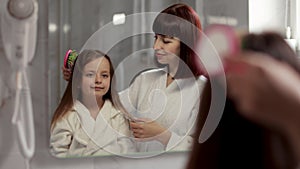 Loving mom brushing hair of cute little girl in the bathroom.