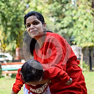 Loving mom carrying of her baby at society park. Bright portrait of happy mum holding child in her hands. Mother hugging her