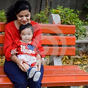 Loving mom carrying of her baby at society park. Bright portrait of happy mum holding child in her hands. Mother hugging her