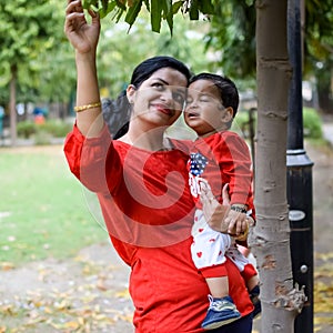 Loving mom carrying of her baby at society park. Bright portrait of happy mum holding child in her hands. Mother hugging her