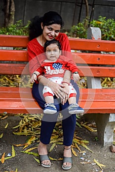 Loving mom carrying of her baby at society park. Bright portrait of happy mum holding child in her hands. Mother hugging her