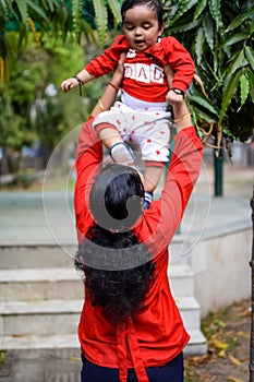 Loving mom carrying of her baby at society park. Bright portrait of happy mum holding child in her hands. Mother hugging her