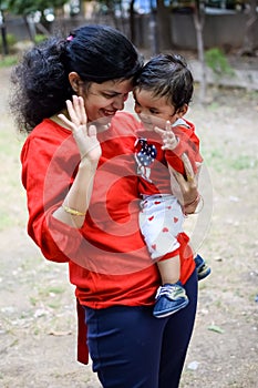 Loving mom carrying of her baby at society park. Bright portrait of happy mum holding child in her hands. Mother hugging her