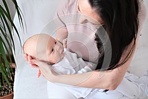 Loving mom carying of her newborn baby at home. Bright portrait of happy mum holding infant child on hands.
