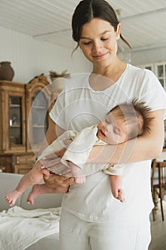 Loving mom carying of her newborn baby at home. Woman holding a baby at the kitchenroom.