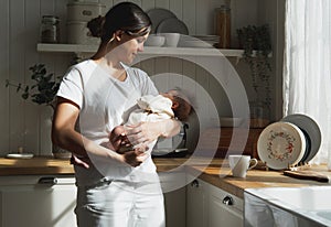 Loving mom carying of her newborn baby at home. Woman holding a baby at the kitchenroom.