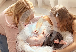 Loving mom and older sister hold the handle of a newborn boy and kiss, cute tiny baby. Portrait a Mom and her baby