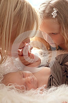 Loving mom and older sister hold the handle of a newborn boy and kiss, cute tiny baby. Portrait a Mom and her baby.