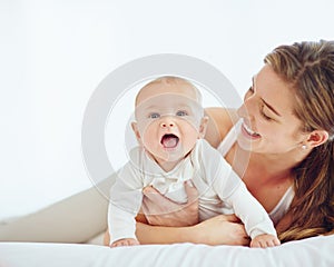 Loving mother and baby bonding at home, playing while relaxing on a bed together. Happy parent being affectionate with