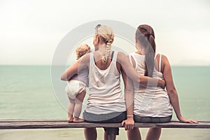 Loving mother embracing her children sitting on wooden bench at tropical beach during vacation. They together looking into the dis