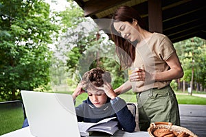 Loving mother helping son to study outdoors