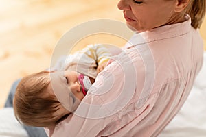 Loving mother holding her little sleeping baby girl on hands, comforting infant kid and looking at child, sitting on bed