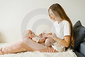 Loving mother holds her newborn baby in her arms at home, sitting on the couch