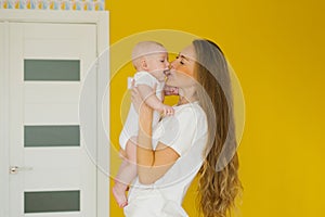 Loving mother holds her newborn baby in her arms at home. A vivid portrait of a happy mother kissing her little son