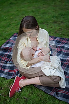 Loving mother hugging her baby and breastfeeds. Picnic in Park with newborn. Vertical frame