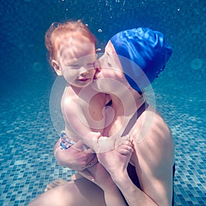 Loving mother kissing baby boy in cheek underwater.